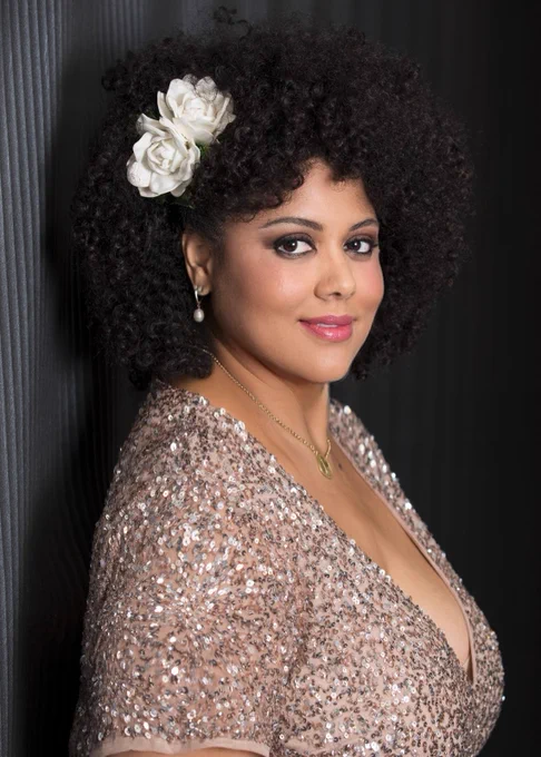 Kim Nalley poses for a portrait photo in a shiny top and a white flower in her hair