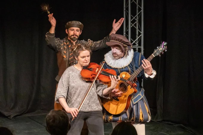 Laura and the musician playing a violin and a guitar while Marlowe conducts.