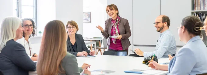 Mehrere lächelnde Personen sitzen im beruflichem Umfeld an einem Tisch. Foto: Landesstelle für die nichtstaatlichen Museen