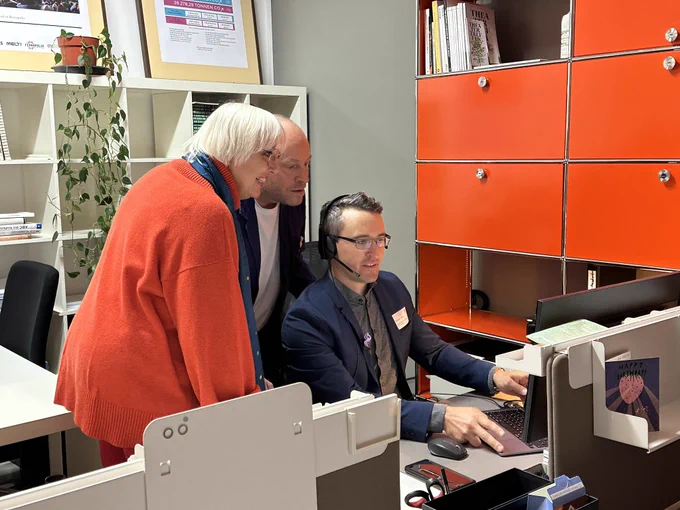 Claudia Roth mit Jacob Bilabel bei einem Mitarbeiter der Green Culture Anlaufstelle an dessen Arbeitsplatz. Sie schauen auf den Computer.