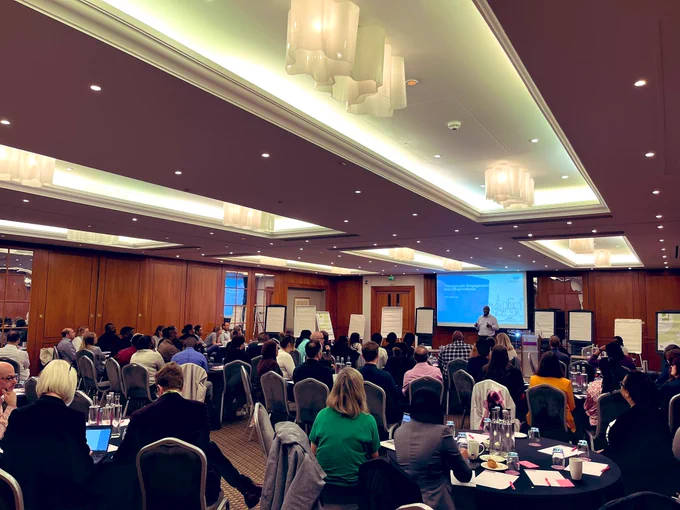 Photo of a room full of people sitting around tables. At the front of the room is a presentation which reads: Therapeutic Engagement and Observations