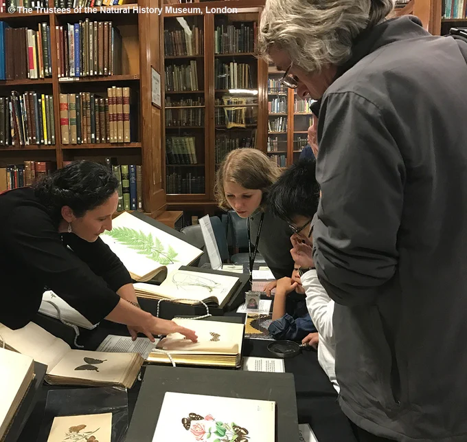 Four adults and a child gathered around a display of rare books and manuscripts, surrounded by wooden bookcases.