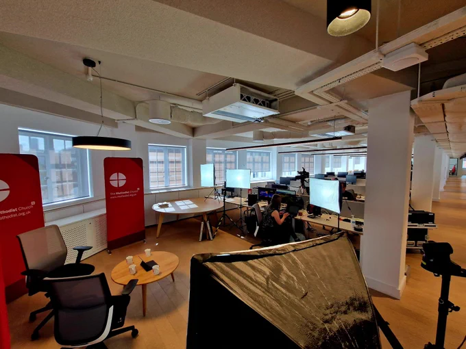 Looking over the top of a light box into a studio area with table and chairs, and Methodist branded banners.