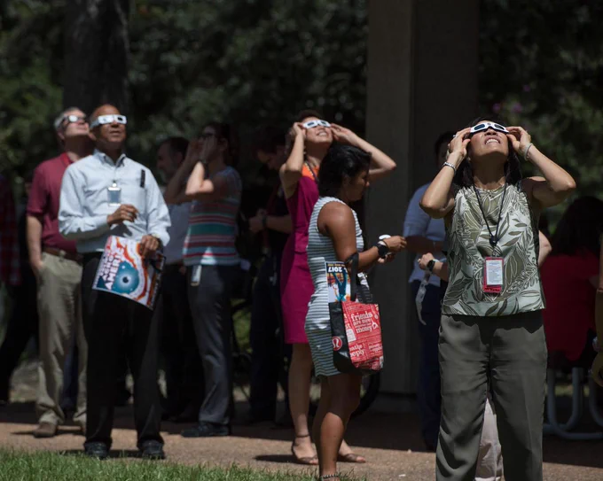 A group of people wearing eclipse glasses and looking toward the sky.