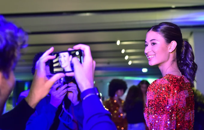 A model in a sequin dress smiles at a person who is holding up their phone to take a photo. Image credit: Julie Howden.