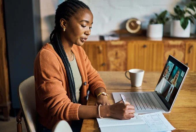 Image of someone working on their laptop at a desk and writing notes.
