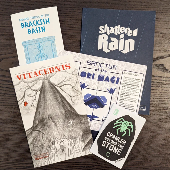 Five print copies of mausritter adventures:
- Drained Temple of the Brackish Basin - a risograph US letter trifold pamphlet, featuring teal colors and an illustration of ambulatory fish reaching toward a glowing crystal
- Shattered Rain - an A5 trifold pamphlet. Logo appears in white over a dark blue background with streaks of rain
- The Vitacernis - An 8x5 risograph zine, the cover has a pencil sketch of a small mouse looking up at a looming tall tree. Vitacernis title appears in scarlet font
- Sanctum of the Ori Magi - A square infinite card with origami illustrations of a weasel, paper cranes, and letters in the logo
- Crawler Beyond the Stone - A small risograph printed pocket mod, features a spider engraved with runes in flourescent green