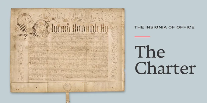 An old yellowed piece of paper with ornate script. Next to the charter are the words "The Insignia of Office. The Charter" 