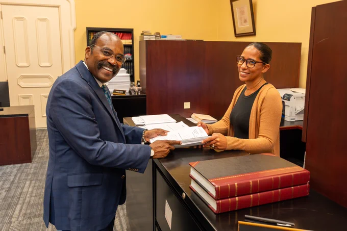 This is a photo of Senator Craig smiling and handing a stack of papers to an employee in the Senate Clerk's office.