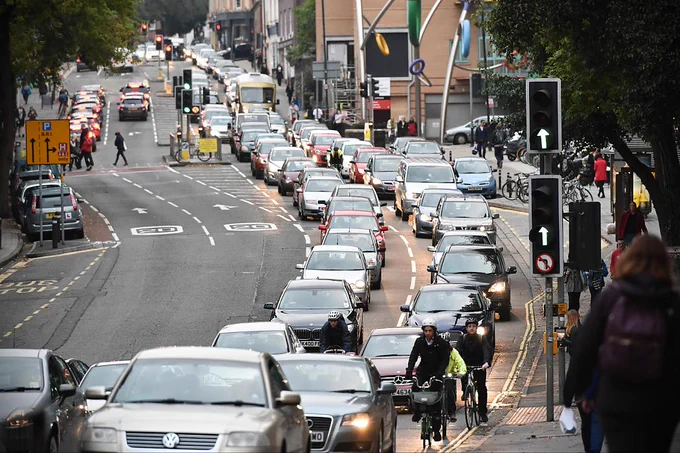 Congestion in an urban area. There are cars and people cycling in the traffic.