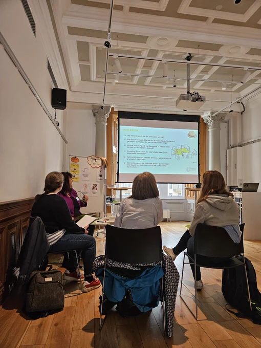 4 people sitting in a classroom with information on a screen in front 