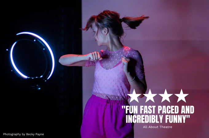 Heather Forster in We Could All Be Perfect. Photo by Becky Payne. A young woman wearing pink is performing a dance routine in front of a ring light. They swish their hair round and hold their hands in fists as they dance.

Quote on top of image reads FOUR STARS "FUN FAST PASED AND INCREDIBLY FUNNY" (All About Theatre)