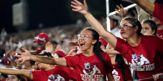 Bulldog Marching Band members in matching red t-shirts cheer on a Fresno State First Down with their arms extended forward.