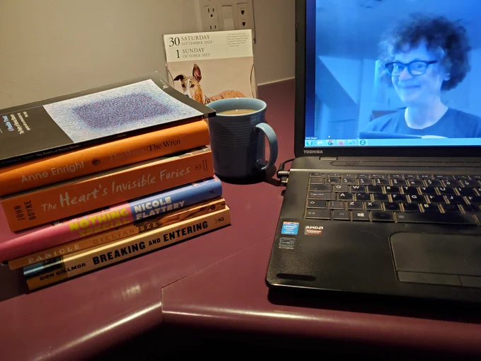 Silent book club member Vicki (that's me, with my signature messy hair and glasses), on screen getting ready for our zoom meeting, with books stacked next to my computer 