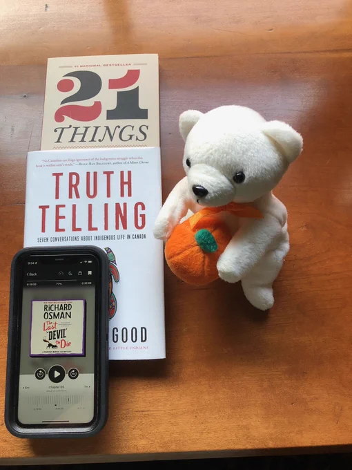 Silent book club member Anne-Louise's recent and current reading, including 21 Things You May Not Know About the Indian Act by Bob Joseph, Truth Telling by Michelle Good and The Last Devil to Die by Richard Osman e-book, accompanied by a white polar bear toy wearing an orange ribbon and holding a plush pumpkin