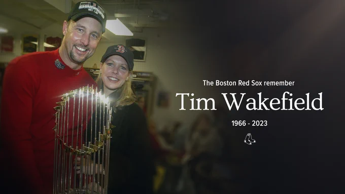 A photo of Tim and Stacy Wakefield posing with the 2004 World Series trophy in the clubhouse after winning. The graphic reads "The Boston Red Sox remember Tim Wakefield 1966-2023"