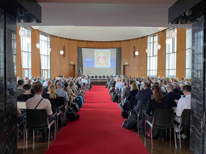 Aula der Uni Freiburg. Menschen hören einem Vortrag zu.