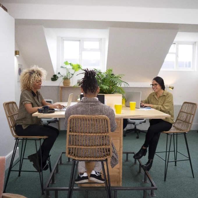 Three people sit around a tall desk in an coworking space