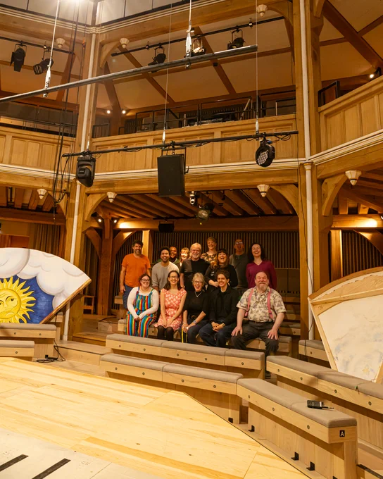 The cast and crew of the Book of Will in the Cockpit at Shakespeare North Playhouse. They're sat on the seats and smiling at the camera