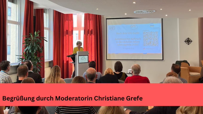 Die Moderatorin steht am Rednerpult und begrüßt die Teilnehmenden