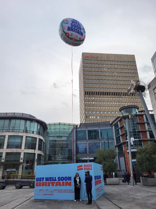 A giant balloon is hoisted in the air in Manchester Exchange Square reading Get Well Soon Britain.