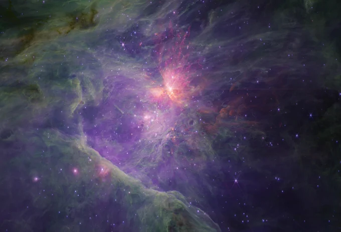 An image of a young star-forming region filled with with wispy purple, green, and red nebulosity. The purple ionised gas is seen mostly towards the centre, with browns, greens, and reds behind, while the periphery is mostly bright green and darker brown to the left. There is a large spray of yellow, orange, red, and purple towards the top centre, and the nebula fades to near black to the right. There are thousands of stars sprinkled across the field, concentrated towards the centre, but they generally appear fainter at longer wavelengths, with some exceptions. The brightest sources in the field have extensive diffraction spikes characteristic of Webb.
