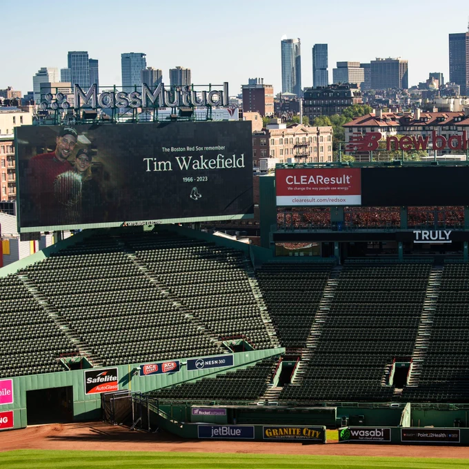 A wide shot of the video boards at Fenway show a graphic with an image of Tim and Stacy Wakefield reading "The Boston Red Sox remember Time Wakefield" on the main video board. 