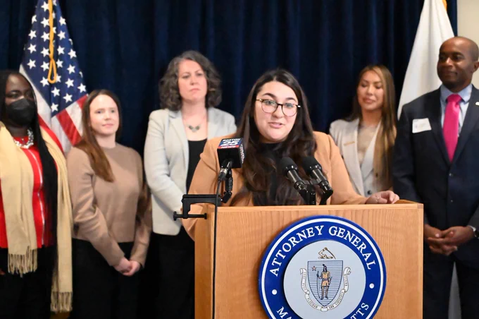 Sapna speaking at a podium with advocates behind her.