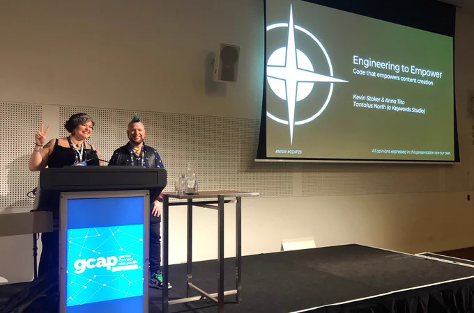 Anna Tito and Kevin Stoker on the GCAP stage in front of their slide show that says "Engineering to Empower - Code that empowers content creation".