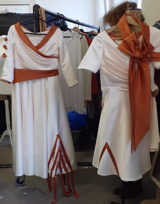 two white dresses with orange trim hung on coat hangers