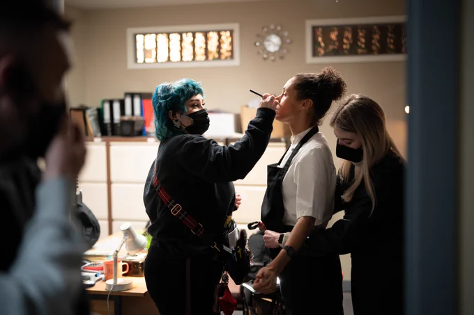 A makeup artist touches up an actor on the set.