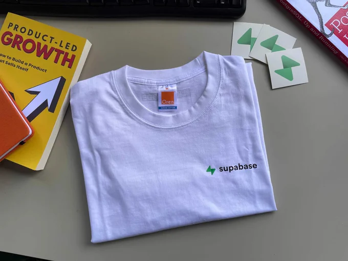 white tee with stickers with the supabase logo 