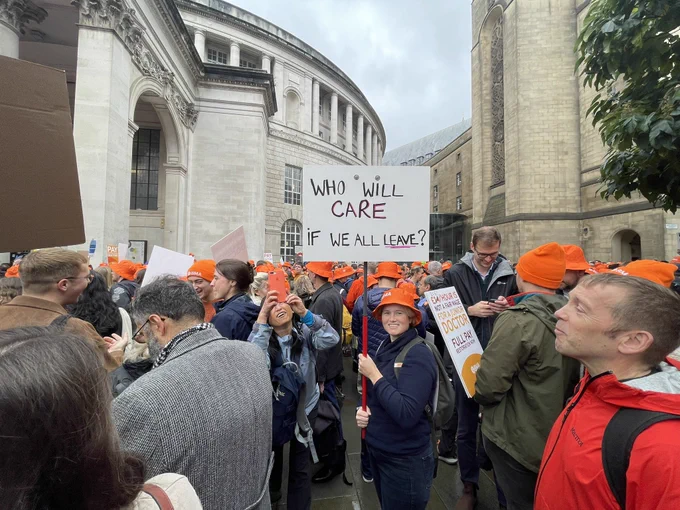 Image of junior doctors and consultants in Manchester with placards and orange BMA hats