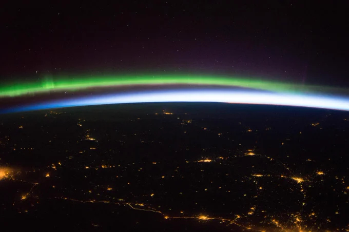An image captured from the International Space Station of Earth sunrise, aurora and sparkling cities in northern Europe. Amongst the top of the image the darkness of space blends into the colorful greens and blues of the aurora. Below the aurora bright sparkling cities are visible in the night. 

Credit: NASA