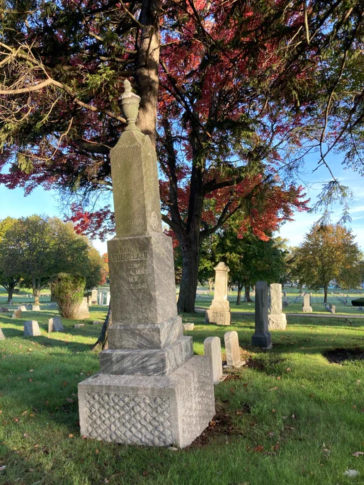 Old cemetery headstones in a line beneath red and green trees.