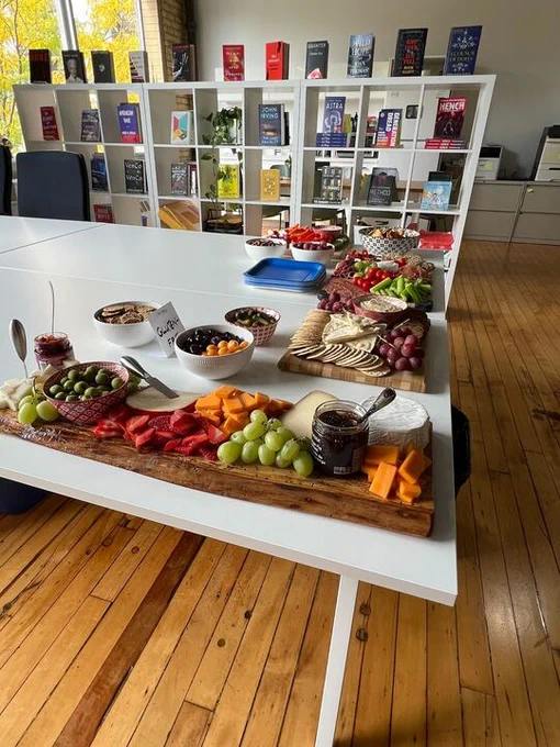 A charcuterie board on a long white table. A shelf full of CMD books is behind the table. 