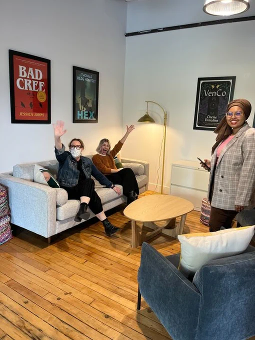 Suzanne Brandreth (with a face mask) and Carolyn Buszynski are on a couch, with the posters for Bad Cree and Hex behind them. Hana El Niwairi is standing across from them, with a poster of VenCo behind her. 