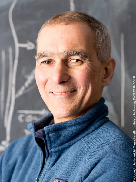 A smiling Moungi Bawendi standing in front of a chalkboard.