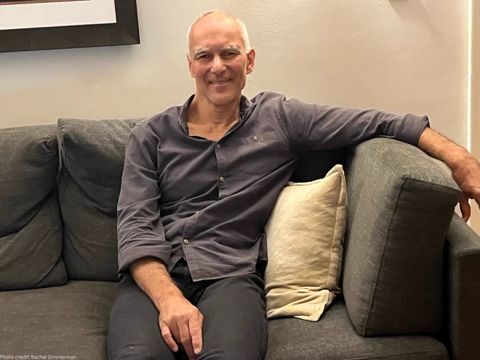 Moungi Bawendi sitting on his couch. He is smiling at the camera.
