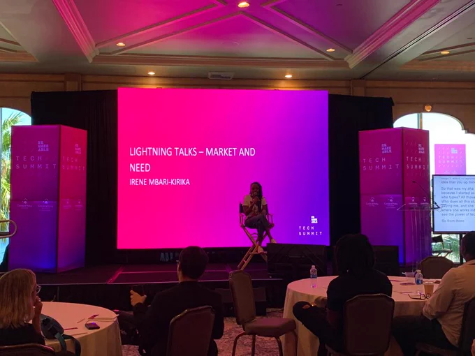 A Picture of Irene Mbari-Kirika seated on a chair on the Remarkable Stage. Behind her, there's a presentation written Lighting Talks - Market and Need, Irene Mbari-Kirika. There are people facing the stage and listening to her.