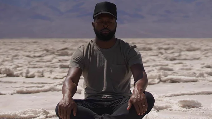 Host Bartunde Thurston is sitting in a mediation pose in the middle of the Utah Salt Flats. 