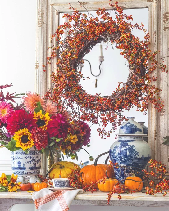 A display of blue-and-white ginger jars and china with pumpkins, red and yellow flowers, and an orange wreath.

