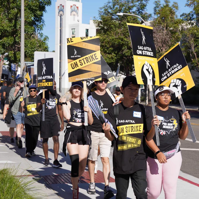 Many people on the picket line holding SAG-AFTRA ON STRIKE signs.