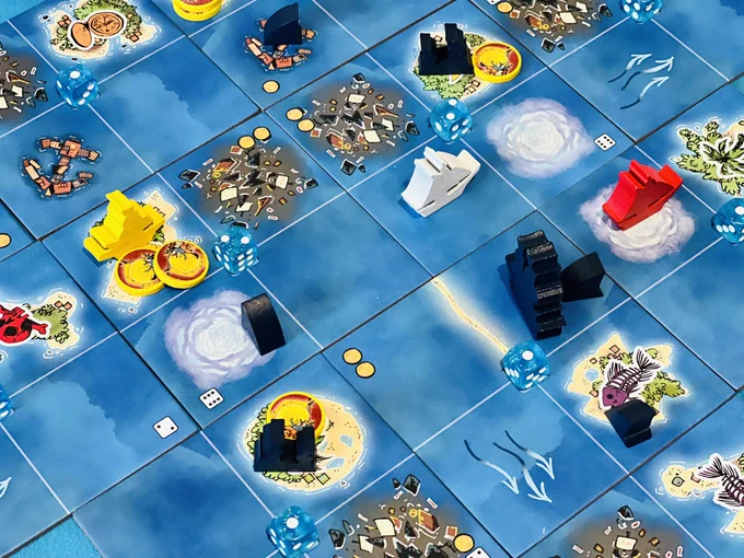 A map of the sea is made of large square tiles split into 4 smaller squares. On some square are images of islands, fog, trash, and harbours. Boats in four colours (red, white, blue, yellow) are on different squares. Wooden shark fin pieces are placed on other tiles, and yellow circle tokens are placed on island spaces.