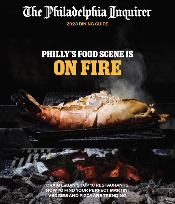The cover of the 2023 Dining Guide, which features lobster cooking over a charcoal fire. Centered white and yellow text says "PHILLY'S FOOD SCENE IS ON FIRE"