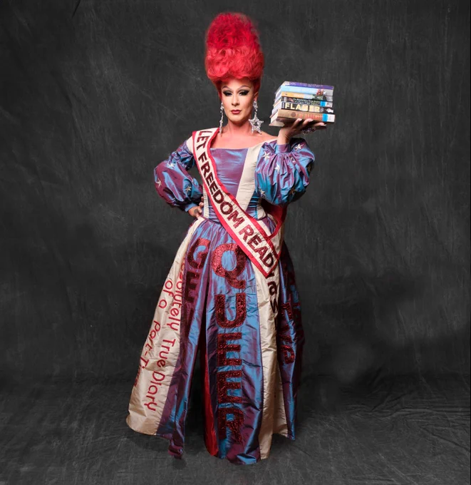 Gia is posing with a stack of banned and challenged books in her hand and a sash that reads Let Freedom Read across the dress. 