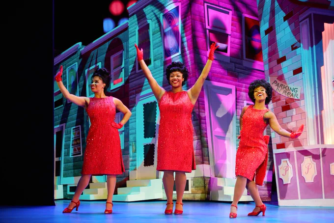 3 performers are on a well-lit stage and they are all dressed in similar red outfits. 