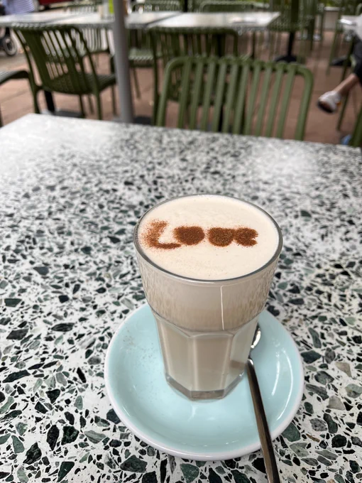 Ein Glas auf einem Tisch mit einem Milchgetränk mit Crema, auf dem mit Zimt geschrieben „LOVE“ steht.