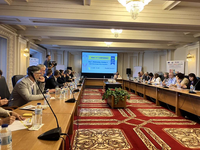 The participants of the EEAC network conference sit around a long table, a presentation on the wall in the background.