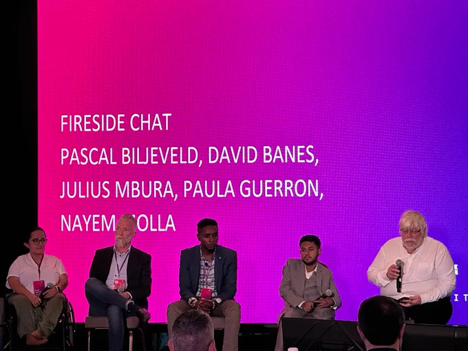 A picture that shows Paula Guerron, Pascal Biljeveld, Julius Mbura, Nayem Molla, and David Bannes seated near each other on a remarkable stage. They are all holding microphones.